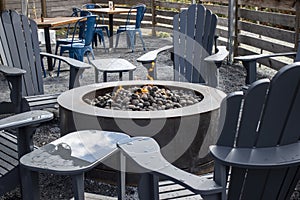 View of adirondack chairs circling a fire pit filled with stones inside an outdoor patio area at a restaurant