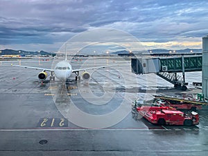 View of an airplane from an airport terminal with a finguer docking for passengers to enter and a special airport vehicle on a