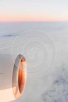 The view from the airplane`s illuminator to the wing, airplane turbine and fluffy clouds at sunrise. Flying over the