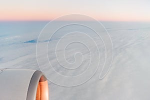 The view from the airplane`s illuminator to the wing, airplane turbine and fluffy clouds at sunrise. Flying over the