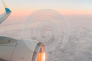 The view from the airplane`s illuminator to the wing, airplane turbine and fluffy clouds at sunrise. Flying over the