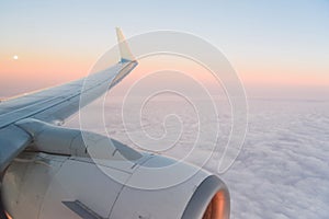 The view from the airplane`s illuminator to the wing, airplane turbine and fluffy clouds at sunrise. Flying over the