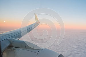 The view from the airplane`s illuminator to the wing, airplane turbine and fluffy clouds at sunrise. Flying over the