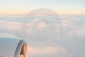 The view from the airplane`s illuminator to the wing, airplane turbine and fluffy clouds at sunrise. Flying over the