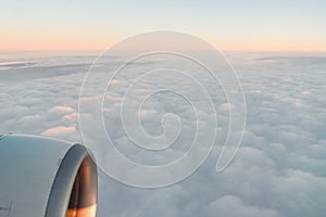 The view from the airplane`s illuminator to the wing, airplane turbine and fluffy clouds at sunrise. Flying over the