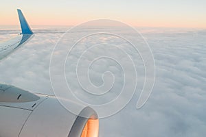 The view from the airplane`s illuminator to the wing, airplane turbine and fluffy clouds at sunrise. Flying over the