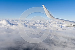 View of airplane white wing flying in blue sky over clouds.