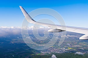 View of airplane white wing flying in blue sky over clouds.