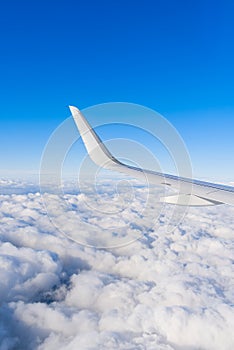 View of airplane white wing flying in blue sky over clouds.