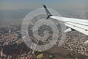View through airplane window of commercial jet plane wing flying high in the sky ove big city. Air travelling concept