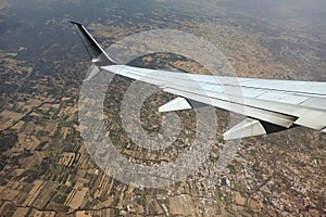 View through airplane window of commercial jet plane wing flying high in the sky ove big city. Air travelling concept