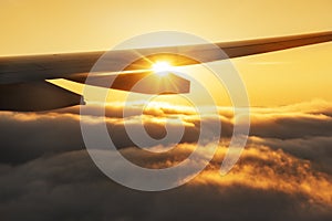 View from an airplane window. Incredible clouds at sunset and the wing of the plane in the rays of the setting sun.