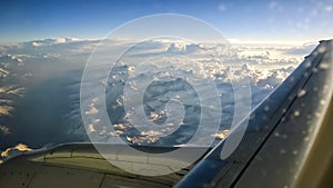 View from airplane window of mountains with snow on the top, clouds, wing and blue sky. For travel concept