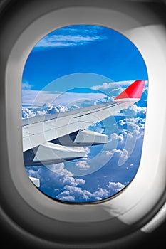 View through airplane window plane flight wing in front of blue white cloud sky. transportation air travel fly concept