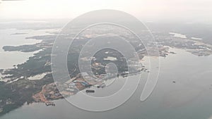 View from airplane window showing houses, buildings, clouds, mountains, skyline, ocean, ships and big boats