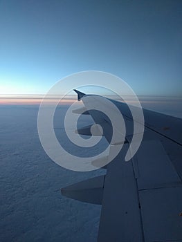 View from airplane window to beautiful sunrise or sunset. Wing of plane and clouds in the sky