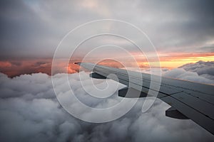 View from the airplane window to thick clouds and a beautiful sunset. Evening flight. The wing of the plane is high