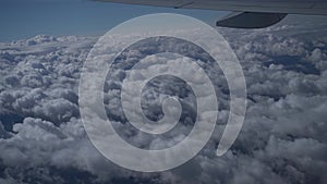 View from airplane window on white fluffy clouds over city on clear sunny day,airplane wing,blue sky.Vacation travel by plane