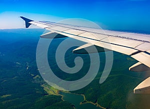 View of airplane wing, blue skies and green land during landing. Airplane window view