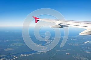 View of an airplane wing, blue sky and green land with a flowing river into a lake during climb