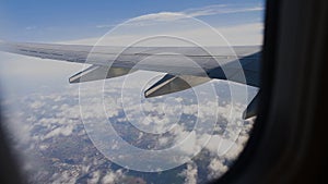 View of airplane wing through plane window. Flying above the clouds.