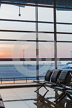 View of airport interoir, empty bench chairs in the departure hall during sunrise. Airplane and building background