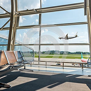 View from the airport lounge to landing plane, passenger aircraft in the sky. Airplane travel concept. Summer vacation