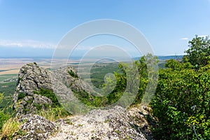 View of the Alazani Valley from a high mountain. Rocks and trees around. Agrarian fields are visible. Clear blue sky and clouds