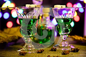 View on alcohol glasses and bottle with green absinthe drink, colorful vibrant bright bokeh background -  binge coma drinking