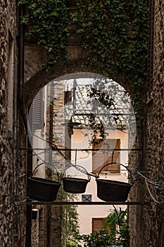 View of an alley in Spello town Umbria, Italy with some old copper pots hanging on the rooftop of an arch