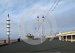 View along the pedestrian promenade in blackpool with traditional wooden shelters and lights with the town buildings in the