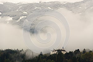 A view of Ambras Castle in Innsbruck, Austria surrounded by trees and against the background of mountains