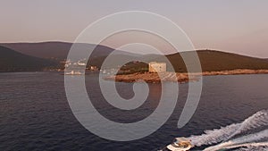 View of the ancient fortress Arza on the Lustica peninsula, Mamula island and motor boat sailing near them at sunset