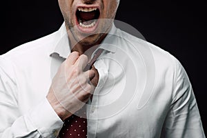 View of angry businessman screaming while touching tie isolated on black