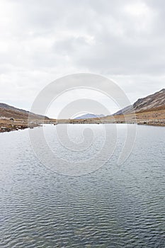 View of another perspective of Lake Tecllo with some hills and rocks in the morning, in Shupluy