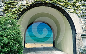 View through an arched gate to a bright beach with unrecognizable people and blue sea, daydream, composition