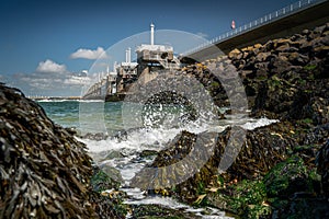 View on the architecture of the flood barrier `Neeltje jans` in the Netherlands from the rocky coast with seaweed and splashing photo