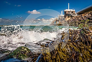 View on the architecture of the flood barrier `Neeltje jans` in the Netherlands from the rocky coast with seaweed and splashing photo