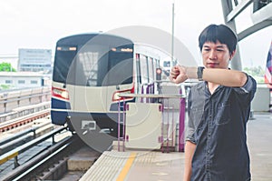 View of asian  man stand and looking at his watch while waiting for something or worrying about time. Motion train as background.