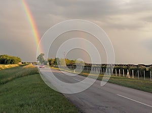 View of the asphalt road with cars and the rainbow above