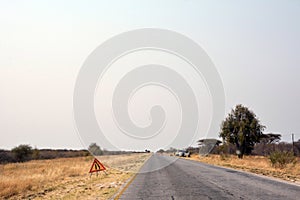 A view of an asphalt road in the desert on which the road is being repaired and warning signs are posted