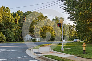 View of an asphalt road with stoplights and green trees on blue sky background. North Carolina.