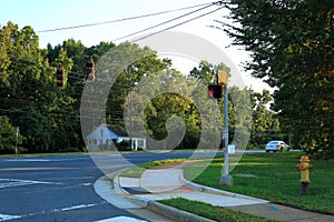 View of an asphalt road with stoplights and green trees on blue sky background. North Carolina