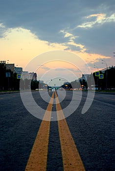 View of an asphalt road with yellow markings closeup and sunset sky in the background.