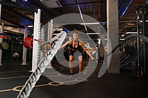 view on athlete woman in gym doing some crossfit exercises using battle ropes.