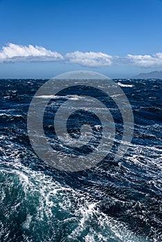 View of Atlantic Ocean and distant mountains, choppy water, calm blue sky with white clouds