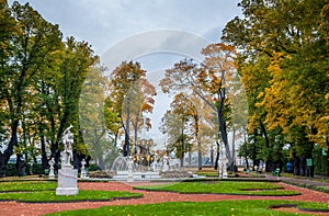 View of autumn trees, ancient marble statues, lawn, fountain and