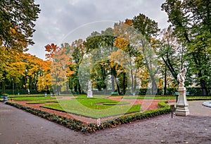 View of autumn trees, ancient marble statues and lawn in Summer