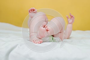 View of the baby from the side of the diaper. The child waves his legs. Pink heels and small fingers of a child up to a