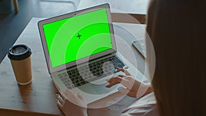 A view from the back of a business woman working in an office interior at a computer and looking at a green screen. An